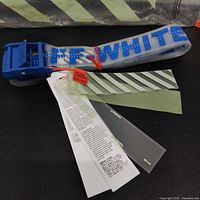 Photo showing the blue Off-White silicone belt coiled, with blue text across strap and original tags and papers laid out.
