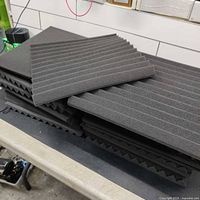 Stack of multiple black foam sound deadening panels with ridged surfaces on a table.