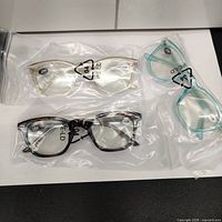 Three pairs of reading glasses sealed in plastic bags with magnification +2.00 and blue light blocking labels.