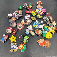 Overview of multiple Crocs charms featuring Nintendo Super Mario Brothers characters, sports, and Harry Potter embellishments arranged on a black surface.
