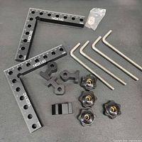 Top view of complete 90 degree positioning squares set with all included components arranged on a flat surface, showing the squares, mounting brackets, knobs, hex keys, clamps, and small washers packed in a bag.