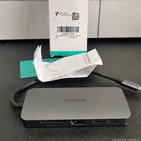 Photo of the MOKiN branded USB-C hub adapter alongside its product box and a folded instruction leaflet on top.