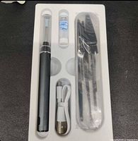 Image of the VITCOCO earwax removal tool and included accessories: device with clear protective cap, cleaning tools in tube, USB charging cable wrapped, and additional items in packaging tray.