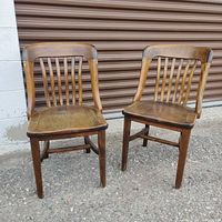 Pair of solid walnut antique chairs with curved top rail and vertical spindle backs, placed on outdoor concrete with metal garage door background