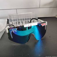 Front view of sunglasses with full reflective blue-to-purple shield lens and white speckled frame placed on a black surface.