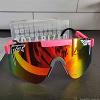 Front view of Pit Viper sunglasses showing reflective multi-color lens with pink and black frame parts.