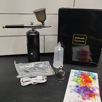 Full lot contents laid out including airbrush compressor, handheld airbrush, paint container, cleaning cap, USB cable, instruction manual and black box