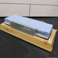 Side angle view of blue whetstone mounted in bamboo base, showing packaging and angle guide.