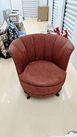 Front view of barrel chair showing rounded back, seat cushion, and suede-like upholstery in brick red color.