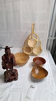 Photo showing all six items: three-slot wicker wine bottle holder, wicker basket, two wooden bowls, one ceramic bowl, and carved wooden figure.