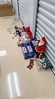 Photo showing entire lot arranged on floor next to storage unit door, includes Santa figure, boxes, mugs, train sets, snowman plushies, candy canes, and string lights.