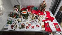 Wide shot showing entire lot of Christmas-themed items on white tablecloth including figurines, tea towels, socks, and ornaments
