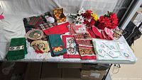 Overview of assorted Christmas linens, holiday-themed towels, napkins, and artificial poinsettia flowers spread on a table.