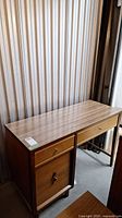 Front view of wooden desk with four drawers and side cabinet, rectangular top surface, metal drawer knobs.