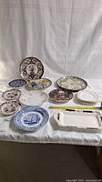 The entire set of decorative plates and the serving tray displayed on a white cloth background showing the variety of plate designs and sizes.