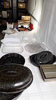 Overview photo showing entire lot: glass Pyrex pans, metal roasting pans with lids, loaf pan, metal racks, and some small kitchen items in background.