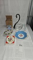 Full view of all items showing coasters in box, swan bowl, crystal vase, blue floral dish, floral platter, and boxed angel candle holder