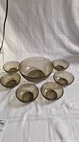 Full view of the vintage Arcoroc glass salad bowl set with one large bowl and six smaller bowls arranged around it on white cloth.