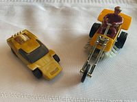 Yellow 1969 Mattel Sizzlers car and yellow 1971 Mattel Chopcycles motorcycle with seated rider on white fabric surface.
