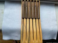 Six Henckels steak knives displayed upright in a wooden holder on white fabric background.