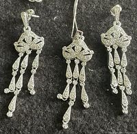Full view of the necklace pendant and two dangling earrings side by side, showing intricate silver and crystal design