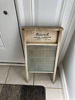 Full view of the antique Rival washboard with wooden frame and ribbed glass scrubbing surface, placed upright on floor against a door.