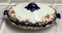 Top and side view of the lidded ceramic dish showing floral and scroll pattern with dark blue trim and handles.