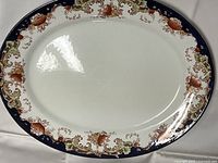 Top view of the oval platter showing decorative floral and scroll border in blue, green, gold, and brown with a white center.