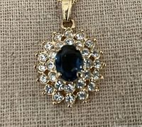 Close-up of oval sapphire blue pendant surrounded by clear round stones set in gold vermeil.