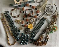 Overall lot showing multiple pieces of costume jewellery including necklaces, bracelets, brooches, and earrings laid on white fabric.