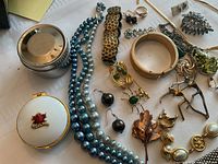 Image showing assortment of costume jewellery including bracelets, earrings, necklaces, pendants, brooches, and trinket holders on a white surface.