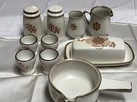 Full lot showing nine pieces laid out on a white surface including salt shaker, pepper shaker, sugar container (missing lid), creamer jug, small pitcher, butter dish, four egg cups, and a pouring bowl.