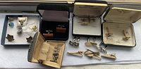 Photo showing assortment of cufflinks, tie clips, and pins in various boxes and loose.