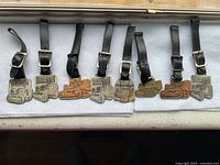 Eight Caterpillar watch fobs with attached black leather straps laid out on white cloth, showing the full lot.