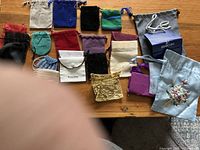 Overview of the lot showing 17 small gift bags of various materials and colors on a wooden surface, including velvet, satin, embroidered, and fabric bags.