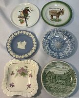 Top view of 6 decorative trinket dishes on fabric background showing variety of designs including bird, floral, scenic, and classical relief.