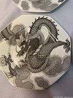 Single detailed view of one octagonal plate featuring a black and gray stylized dragon with clouds