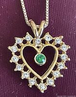 Close-up of heart-shaped pendant with clear stones surrounding and a green stone in the center.