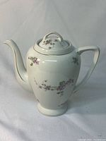 Full side view showing shape, handle, spout, lid, and floral decoration of the white porcelain pot.