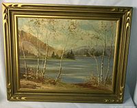 Full view of the framed oil on board landscape painting showing lake, trees, and distant mountains in a gold decorative frame.