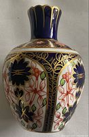 Porcelain vase showing detailed blue, red, green, and gold Imari floral pattern with scalloped top edge.