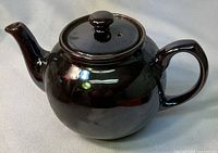 Front and side view of brown glazed ceramic teapot with bulbous shape and handle.