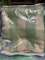 Photo of folded green and cream checkered wool blanket in plastic covering with Skelton Wool Scotland label visible