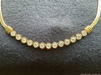 Close-up photo of the necklace's central curved bar featuring 11 clear round Swarovski crystals set in gold-tone bezels.