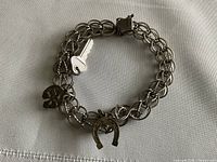 Vintage sterling silver charm bracelet with three charms on white fabric background.