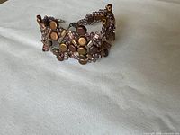 Close-up photo of one Baroque style bracelet with glass beads and crystal beads in metallic and purple tones laid flat on a white surface.