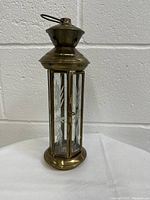 Full view of vintage brass and glass candle lantern upright against white brick wall.