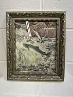Front view of framed vintage print showing two Atlantic salmon jumping over rocky river water. Ornate metallic finish frame with floral carvings.