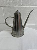 Front and side profile view of stainless steel teapot showing handle, lid with finial, and long spout