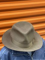 Brown felt fedora hat with crease crown and wide brim, placed on a blue jacket.